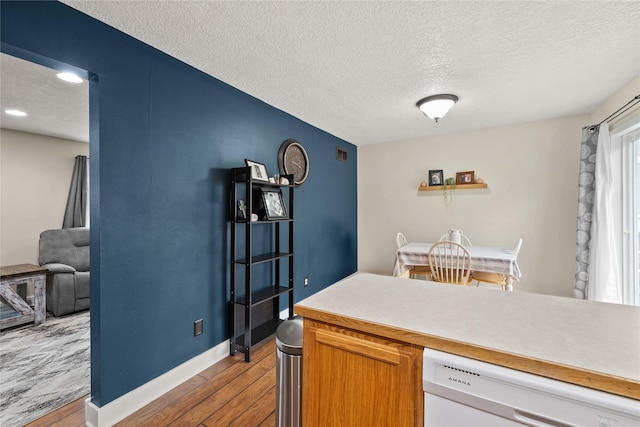 kitchen with light countertops, white dishwasher, a textured ceiling, wood finished floors, and baseboards