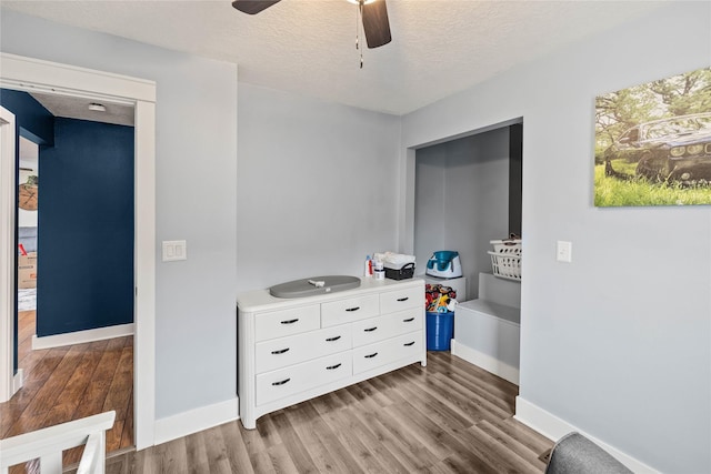 interior space with ceiling fan, a textured ceiling, baseboards, and wood finished floors