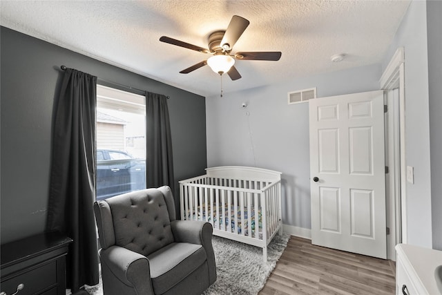 bedroom with a textured ceiling, visible vents, a ceiling fan, light wood-type flooring, and a crib