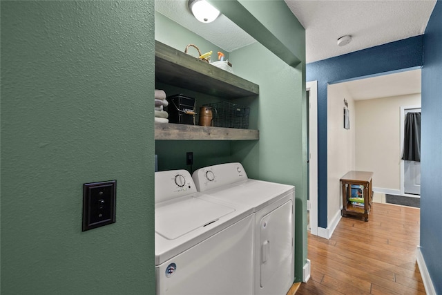 washroom with laundry area, washing machine and dryer, hardwood / wood-style flooring, and baseboards