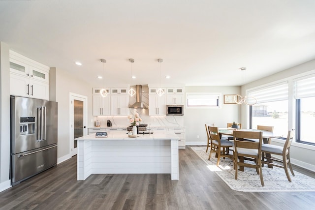 kitchen featuring a kitchen island with sink, stainless steel appliances, light countertops, backsplash, and wall chimney exhaust hood