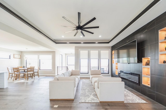 unfurnished living room with recessed lighting, a raised ceiling, a tiled fireplace, and wood finished floors