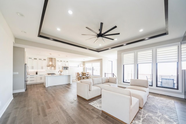 unfurnished living room featuring baseboards, a ceiling fan, wood finished floors, a tray ceiling, and recessed lighting