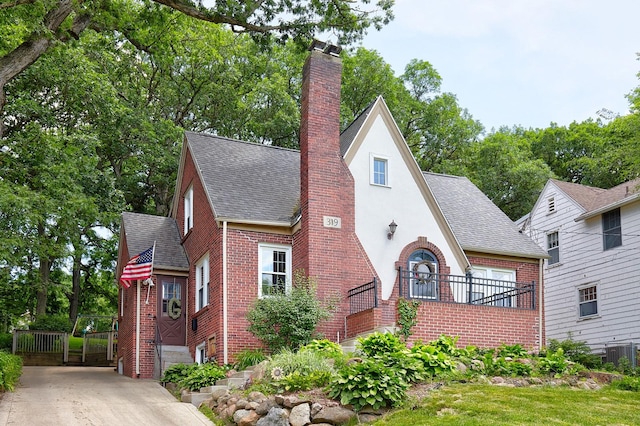 tudor home with stucco siding, central AC, a shingled roof, brick siding, and a chimney