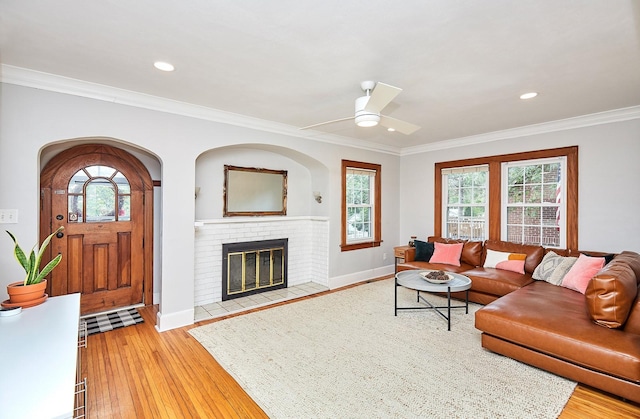 living area with light wood-style floors, crown molding, a fireplace, and a wealth of natural light