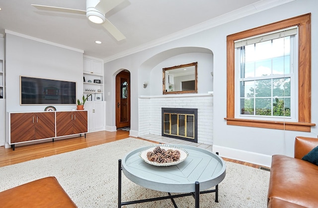 living area with ornamental molding, a brick fireplace, wood finished floors, and baseboards