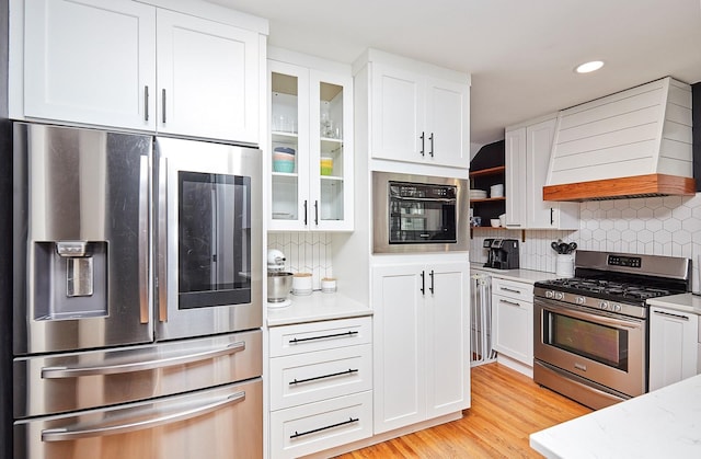 kitchen with custom exhaust hood, open shelves, stainless steel appliances, decorative backsplash, and white cabinets