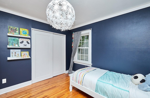 bedroom with a chandelier, wood finished floors, baseboards, ornamental molding, and a closet