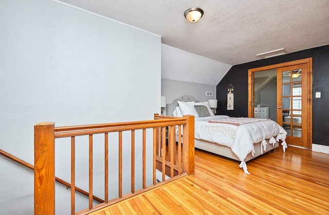 bedroom with a textured ceiling, visible vents, vaulted ceiling, and wood finished floors