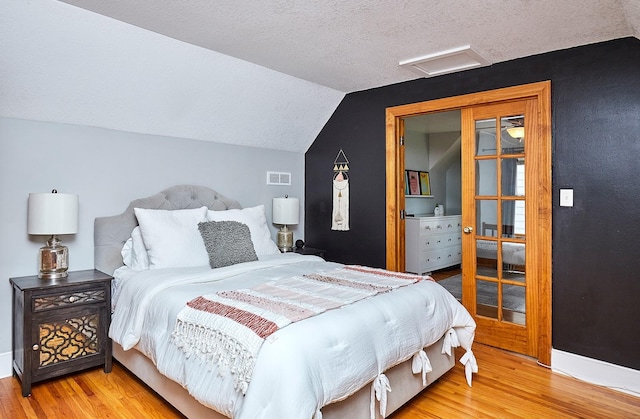 bedroom featuring light wood finished floors, visible vents, attic access, vaulted ceiling, and a textured ceiling