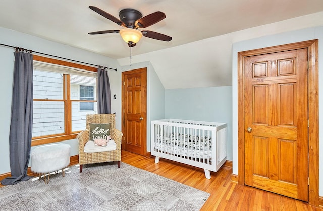 bedroom featuring lofted ceiling, ceiling fan, wood finished floors, a nursery area, and baseboards