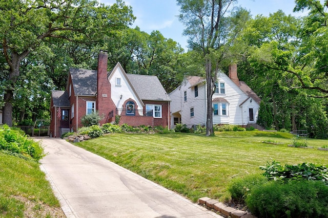 tudor home with a front lawn, brick siding, and a chimney