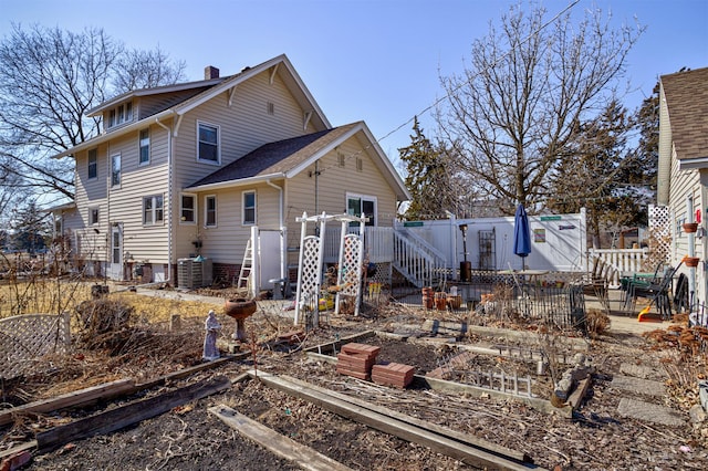 rear view of house featuring a deck, central AC unit, fence, a vegetable garden, and a chimney