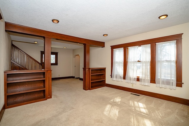 carpeted empty room featuring baseboards, visible vents, arched walkways, stairway, and a textured ceiling