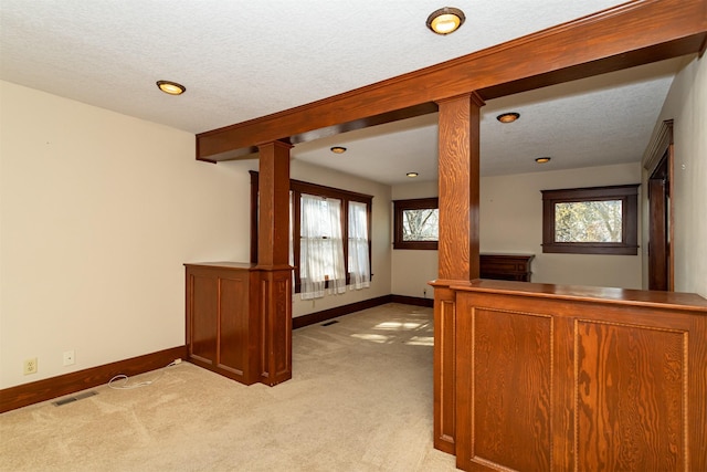 interior space with a wealth of natural light, light carpet, decorative columns, and baseboards