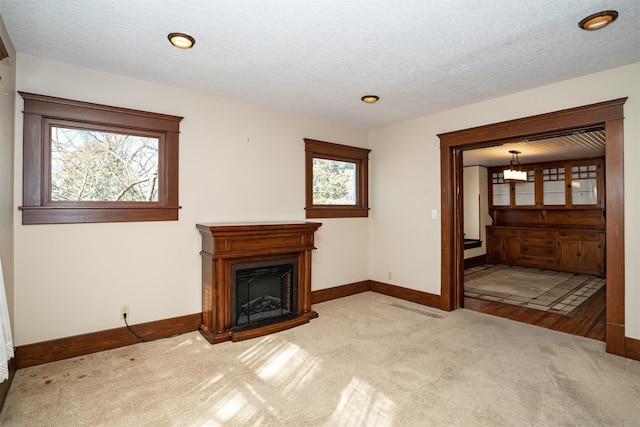 unfurnished living room with a fireplace, light colored carpet, visible vents, a textured ceiling, and baseboards