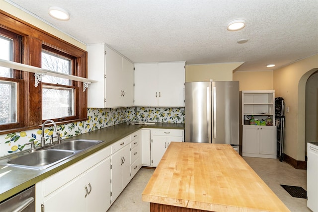 kitchen with arched walkways, stainless steel appliances, white cabinetry, a sink, and butcher block countertops