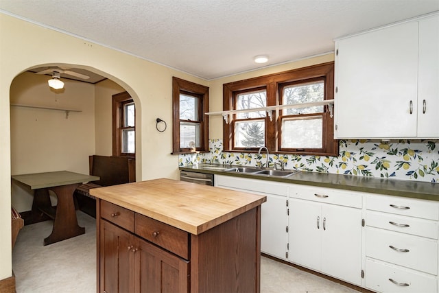 kitchen with arched walkways, white cabinets, a textured ceiling, wooden counters, and a sink