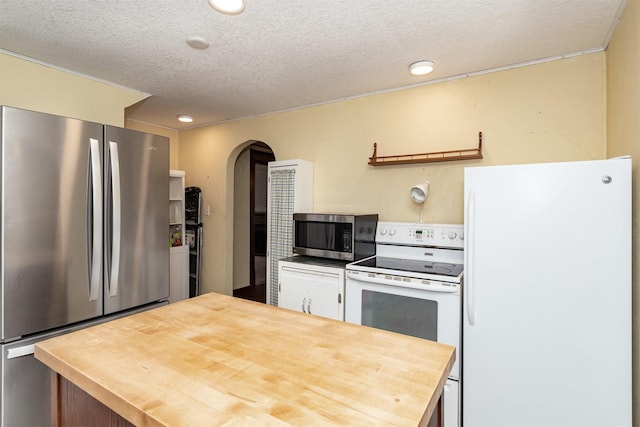 kitchen with stainless steel appliances, arched walkways, butcher block countertops, and a textured ceiling