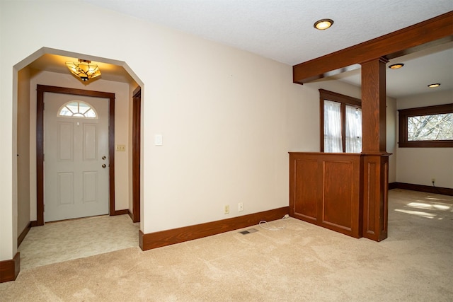 entrance foyer with light carpet, baseboards, arched walkways, and beam ceiling