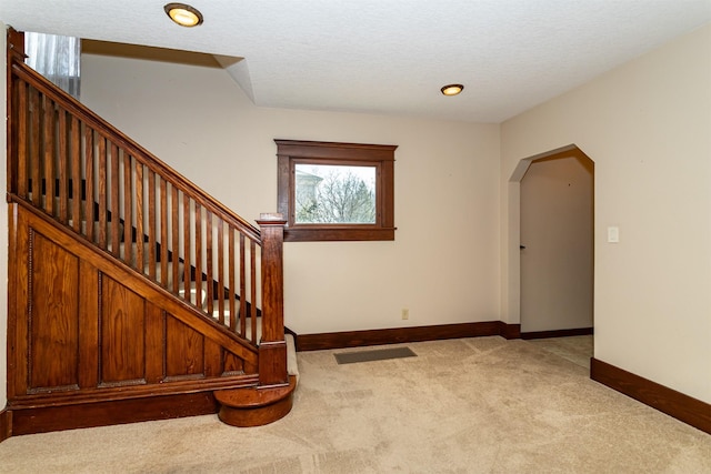 stairs featuring arched walkways, a textured ceiling, carpet flooring, and baseboards