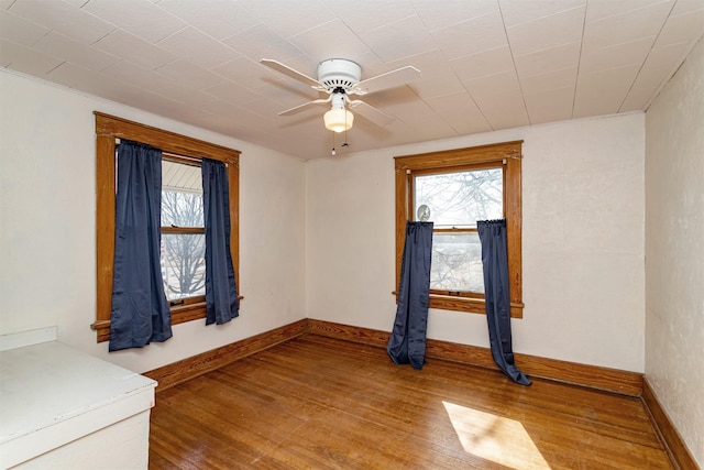 spare room featuring plenty of natural light, wood-type flooring, a ceiling fan, and baseboards