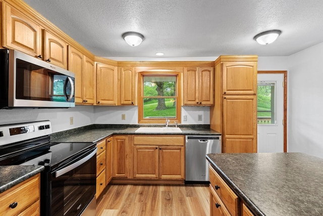 kitchen with stainless steel appliances, dark countertops, a sink, and light wood-style flooring