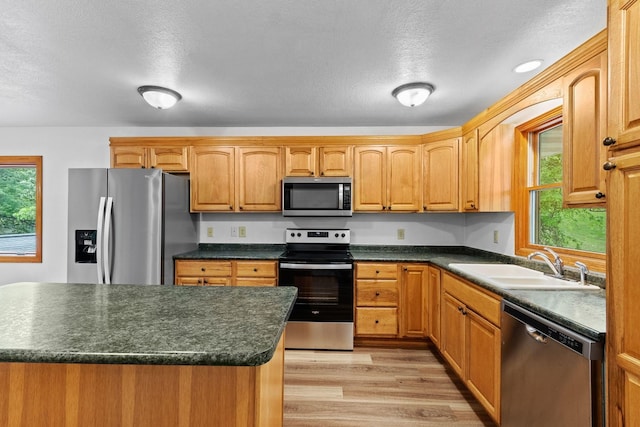 kitchen featuring stainless steel appliances, dark countertops, light wood-style flooring, a sink, and a textured ceiling