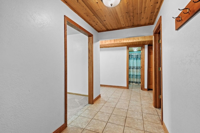 hall featuring light tile patterned floors, a textured wall, wooden ceiling, and baseboards