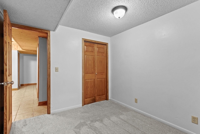 unfurnished bedroom with a closet, light carpet, a textured ceiling, and baseboards