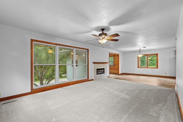 unfurnished living room with carpet, a textured ceiling, a tiled fireplace, and baseboards