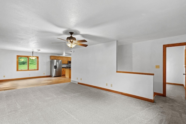 unfurnished living room with a textured ceiling, baseboards, and a ceiling fan