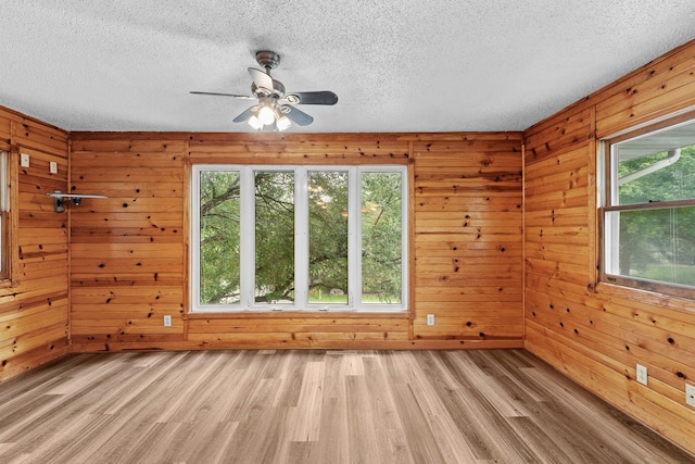 empty room featuring a textured ceiling, wood walls, light wood-style flooring, and a ceiling fan