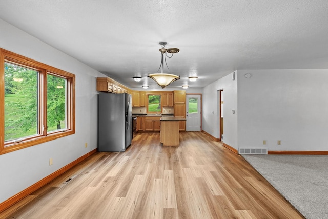 kitchen with visible vents, baseboards, dark countertops, light wood-style flooring, and stainless steel refrigerator with ice dispenser