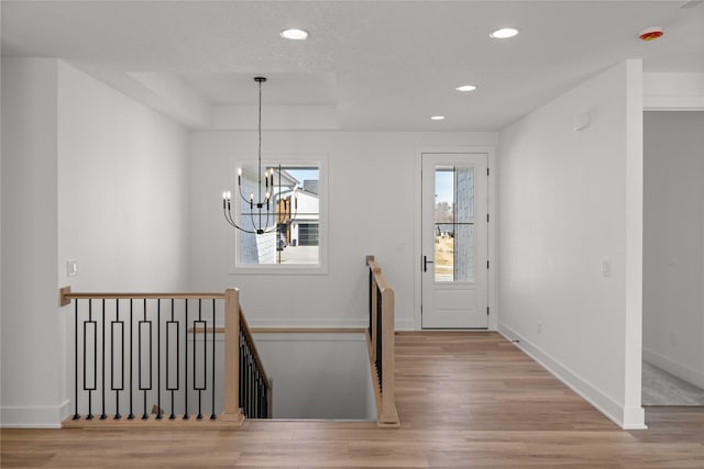 foyer entrance with baseboards, a chandelier, recessed lighting, wood finished floors, and a raised ceiling