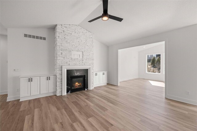 unfurnished living room with a stone fireplace, lofted ceiling, visible vents, and light wood-type flooring