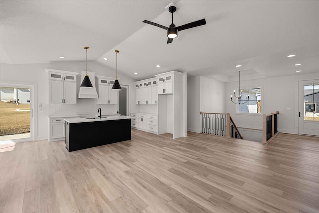 kitchen featuring light wood-style flooring, an island with sink, a sink, light countertops, and vaulted ceiling