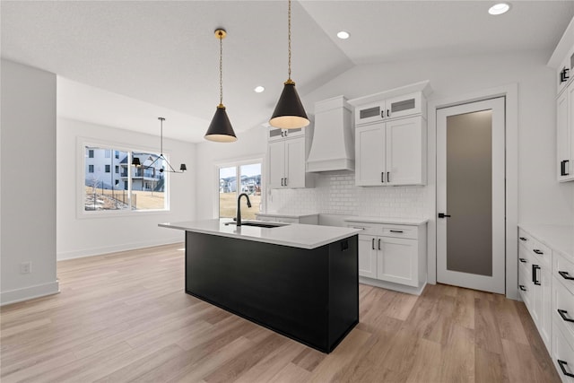 kitchen with premium range hood, a sink, decorative backsplash, vaulted ceiling, and light wood-type flooring