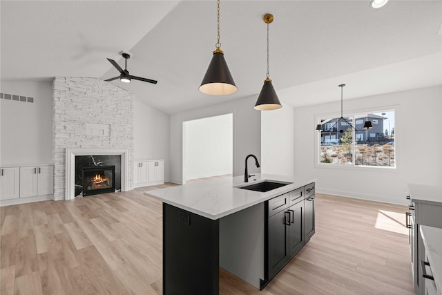 kitchen featuring visible vents, a sink, a stone fireplace, light wood-style floors, and open floor plan