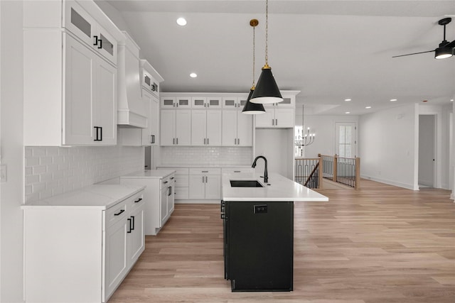 kitchen with glass insert cabinets, an island with sink, light wood-style floors, and a sink