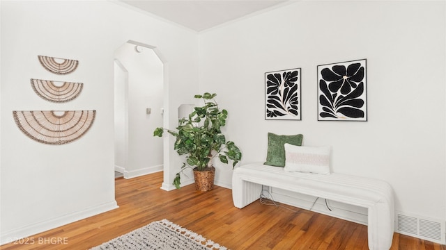 sitting room featuring wood finished floors, visible vents, baseboards, arched walkways, and crown molding