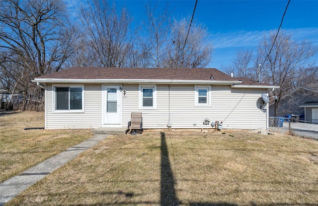 rear view of property featuring a shingled roof, a lawn, and fence