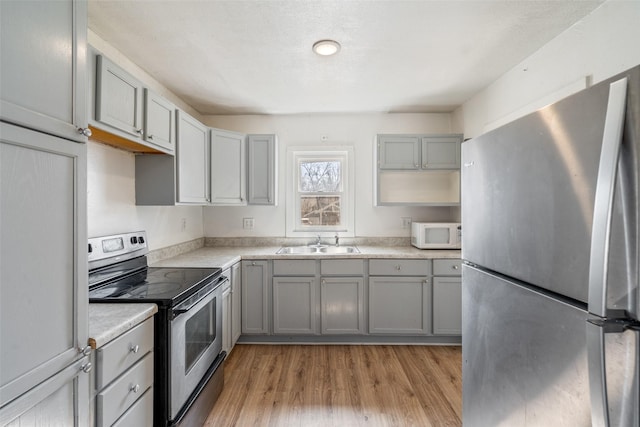 kitchen featuring light wood-type flooring, appliances with stainless steel finishes, gray cabinets, and a sink