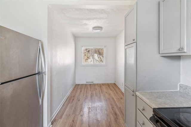 kitchen featuring visible vents, light wood-style flooring, freestanding refrigerator, light countertops, and a textured ceiling