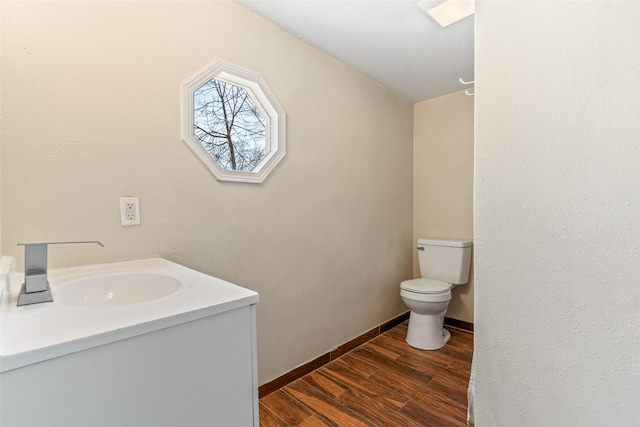 bathroom with toilet, baseboards, wood finished floors, and vanity