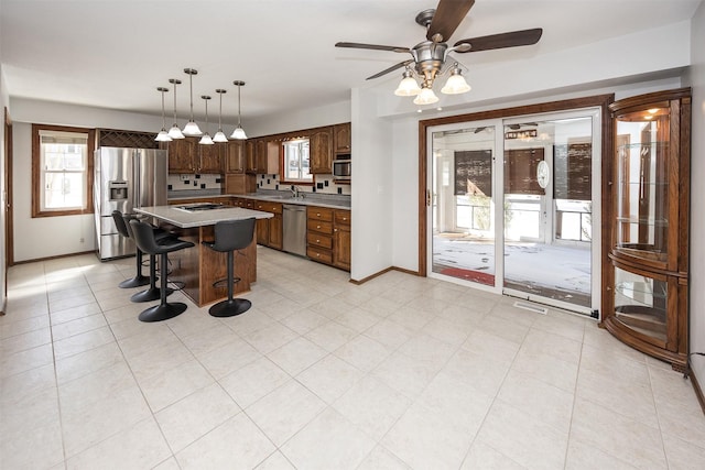 kitchen with baseboards, appliances with stainless steel finishes, a breakfast bar, a center island, and a sink