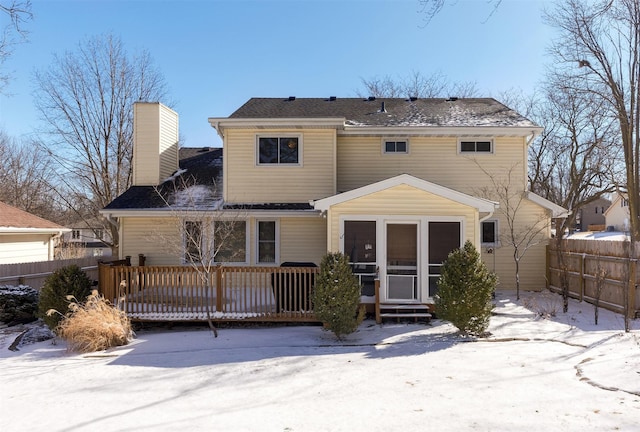 snow covered house with a deck, a chimney, and fence