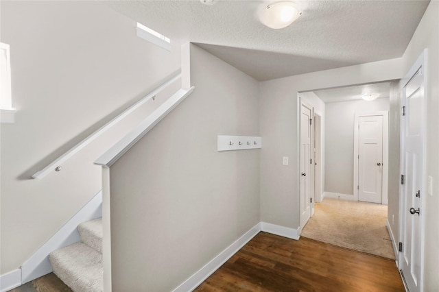 hall featuring a textured ceiling, stairway, wood finished floors, and baseboards