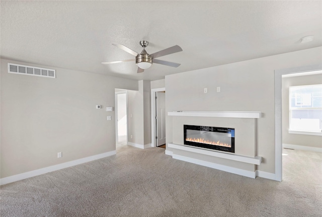 unfurnished living room featuring carpet floors, a ceiling fan, visible vents, baseboards, and a glass covered fireplace