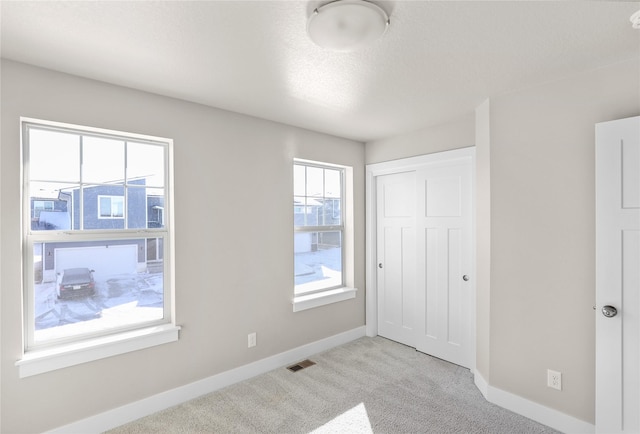 unfurnished bedroom with visible vents, baseboards, carpet, a textured ceiling, and a closet